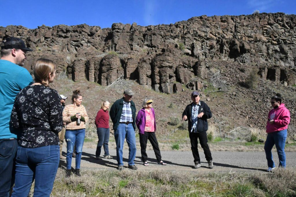 Tribal elder and storyteller Randy Lewis stands in front of the “Singing Rocks” of Moses Coulee, explaining how they absorbed the voices of his people and how those voices can still be heard – if the conditions are right. (Dominick Bonny / Crosscut)
