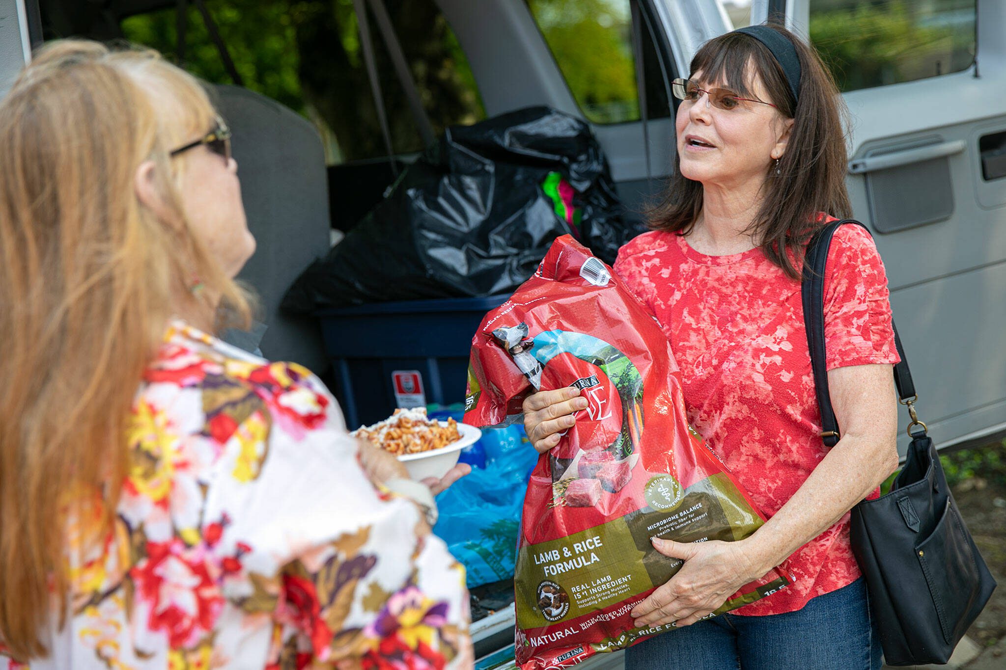 Penelope Protheroe, President and Founder of Angel Resource Connection carries a bag of dog food over to a person’s car while helping distribute food and other supplies on Wednesday, May 17, 2023, in Everett, Washington. (Ryan Berry / The Herald)