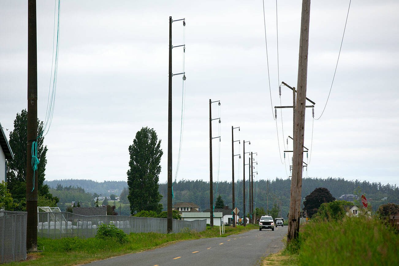 A PUD vehicle drives along Lovers Road under newly-erected power poles that will eventually connect Stanwood and Camano Island on Tuesday, May 30, 2023, in Stanwood, Washington. (Ryan Berry / The Herald)