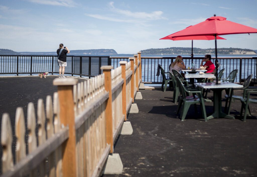 A person takes a photograph of the water from the new parklet while people dine at the new table additions at the parklet for Ivar’s on Thursday, Aug. 5, 2021 in Mukilteo, Washington. (Olivia Vanni / The Herald) 
