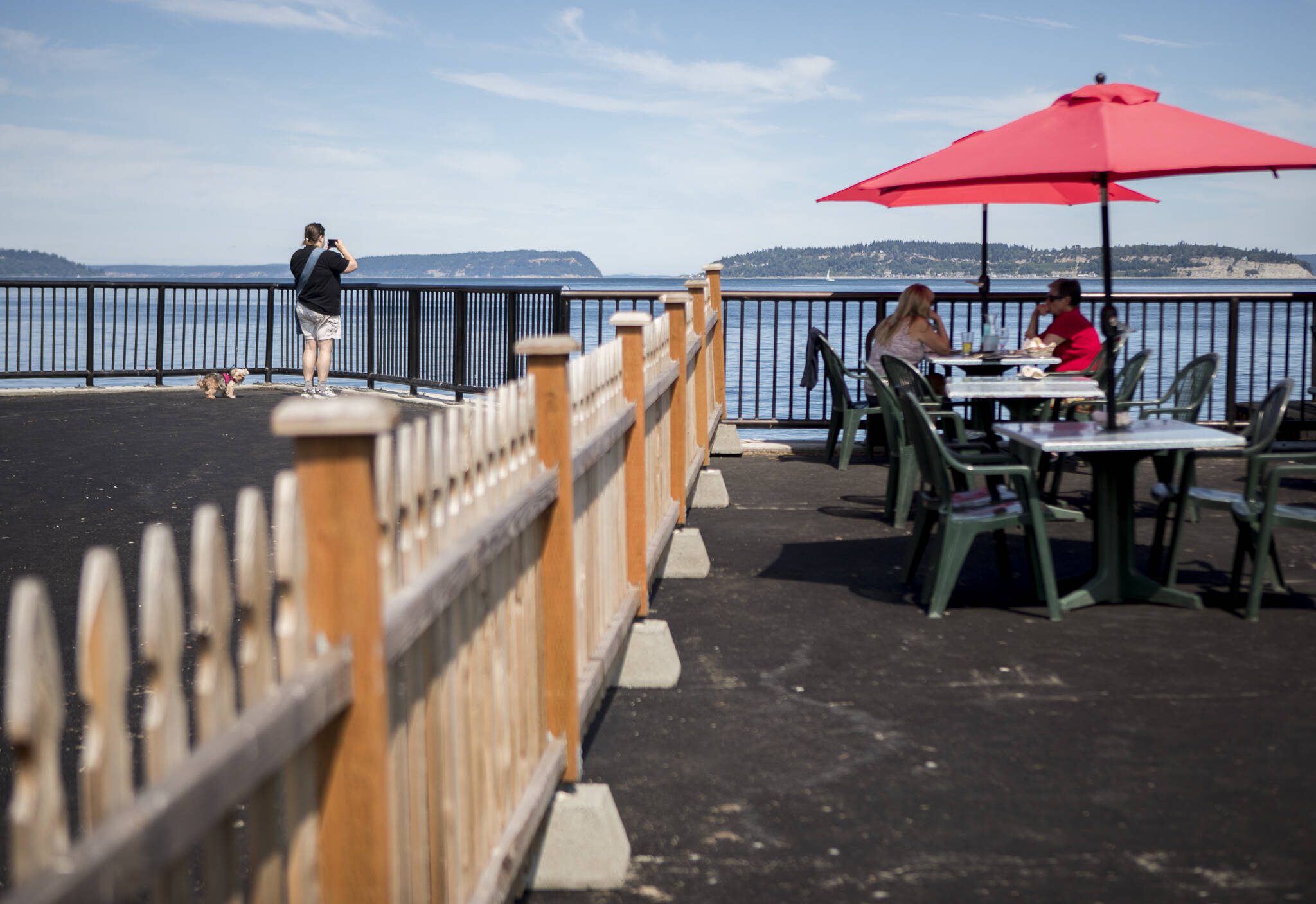 A person takes a photograph of the water from the new parklet while people dine at the new table additions at the parklet for Ivar’s on Thursday, Aug. 5, 2021 in Mukilteo, Washington. (Olivia Vanni / The Herald)