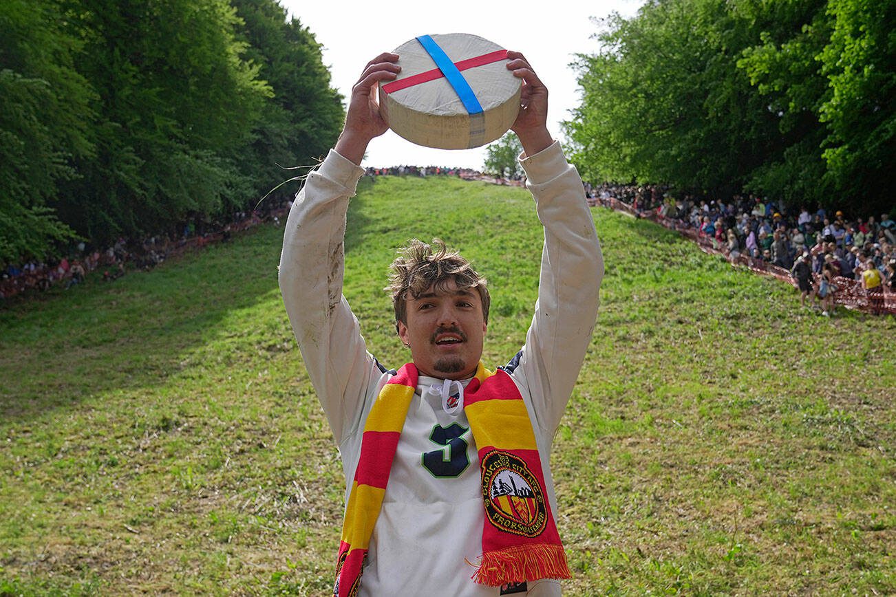 Cooper Cummings from the United States celebrates after winning a men's downhill during the Cheese Rolling contest at Cooper's Hill in Brockworth, Gloucestershire, Monday May 29, 2023. The Cooper's Hill Cheese-Rolling and Wake is an annual event where participants race down the 200-yard (180 m) long hill chasing a wheel of double gloucester cheese. (AP Photo/Kin Cheung)