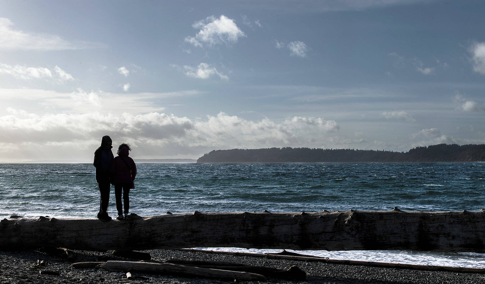 A couple stands on a large piece of driftwood in the wind at Mukilteo Lighthouse Park on Friday, Jan. 4, 2018 in Mukilteo, Wa. There is a small craft advisory in effect until 10 pm Friday. (Olivia Vanni / The Herald)