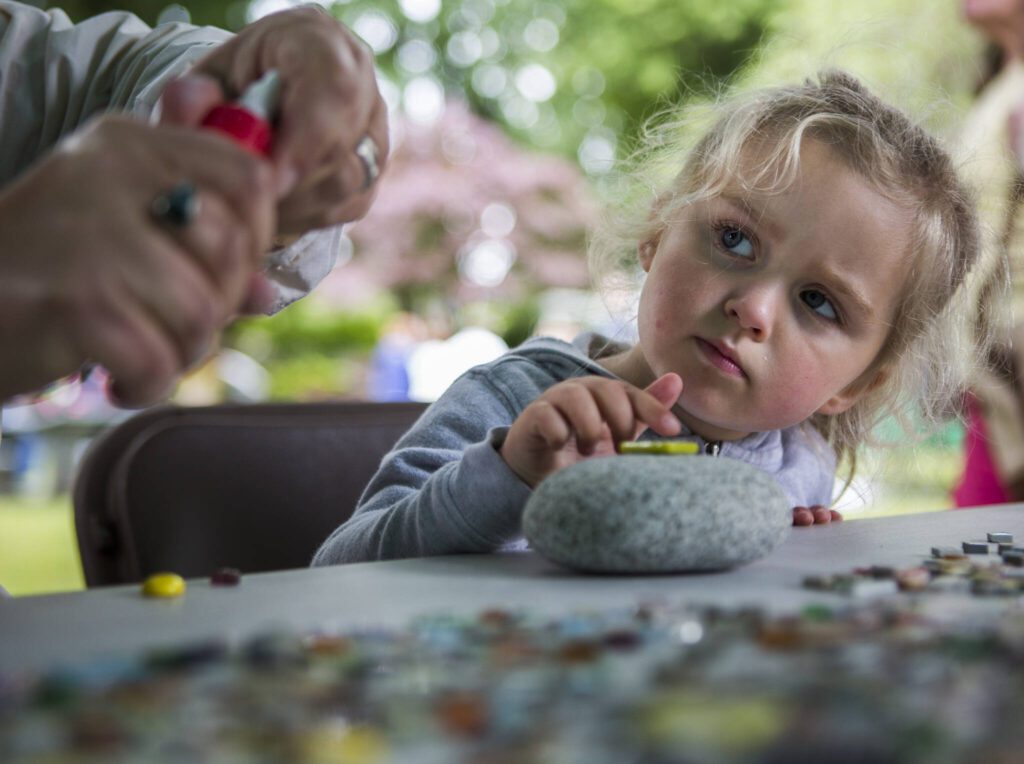 Ella Snitily, 3, watches her grandma as she works on decorating a stone during Sorticulture at Legion Memorial Park on Friday, June 7, 2019 in Everett, Wa. (Olivia Vanni / The Herald)
