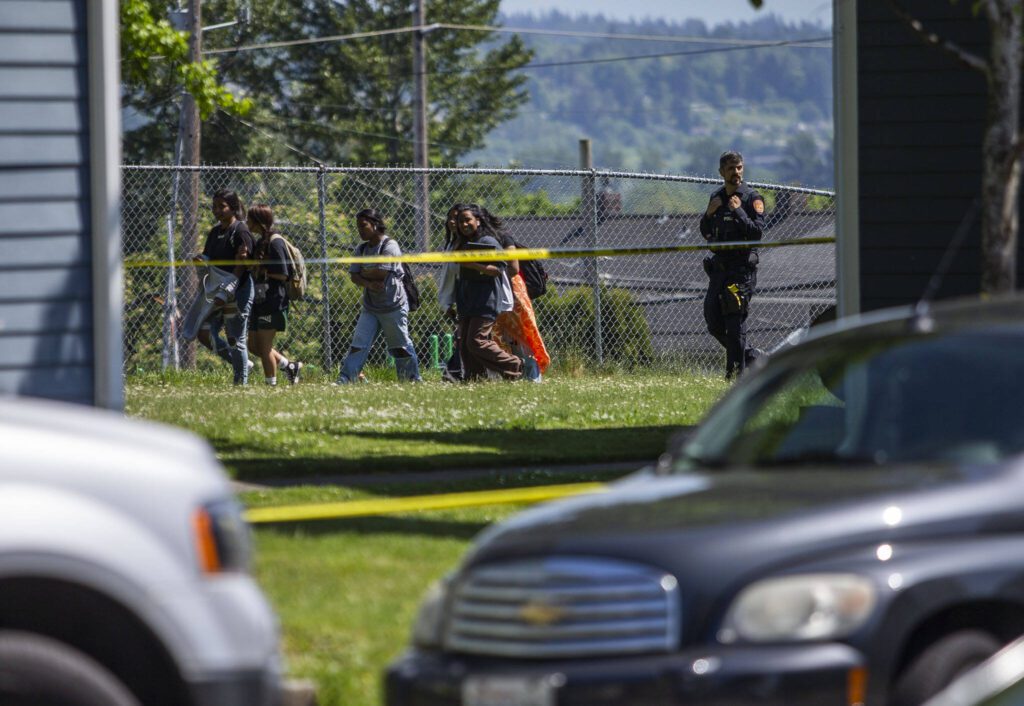 A police officer escorts kids just released from school around the crime scene along Linden Street on Friday, May 19, 2023 in Everett, Washington. (Olivia Vanni / The Herald)
