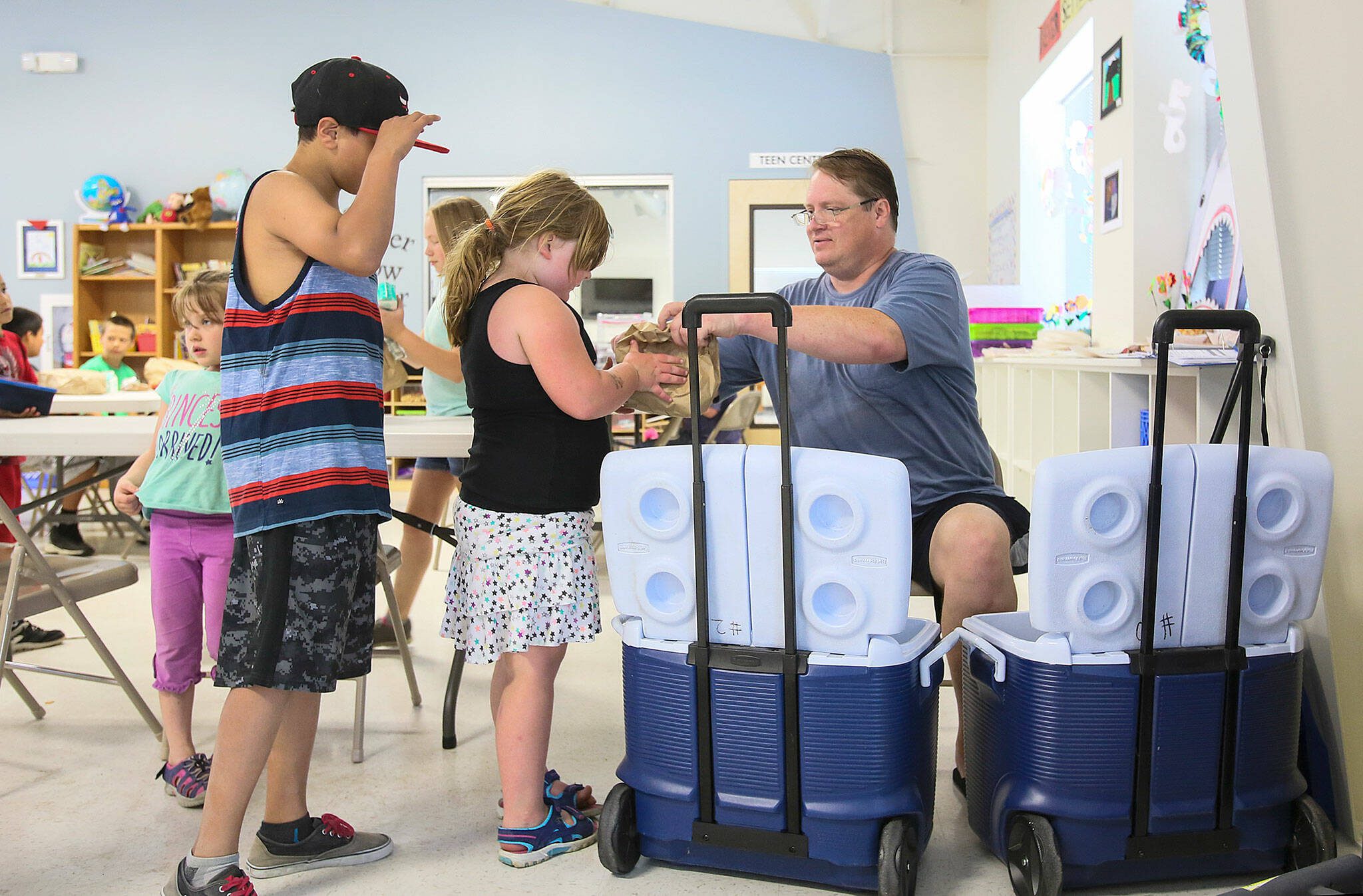 From one of two coolers, Mike Bradshaw-Heiberg hands out brown bag lunches and half pints of milk as part of the Kids Cafe summer meals program on July 1, 2015 in Sultan, Washington. (Kevin Clark / The Herald)