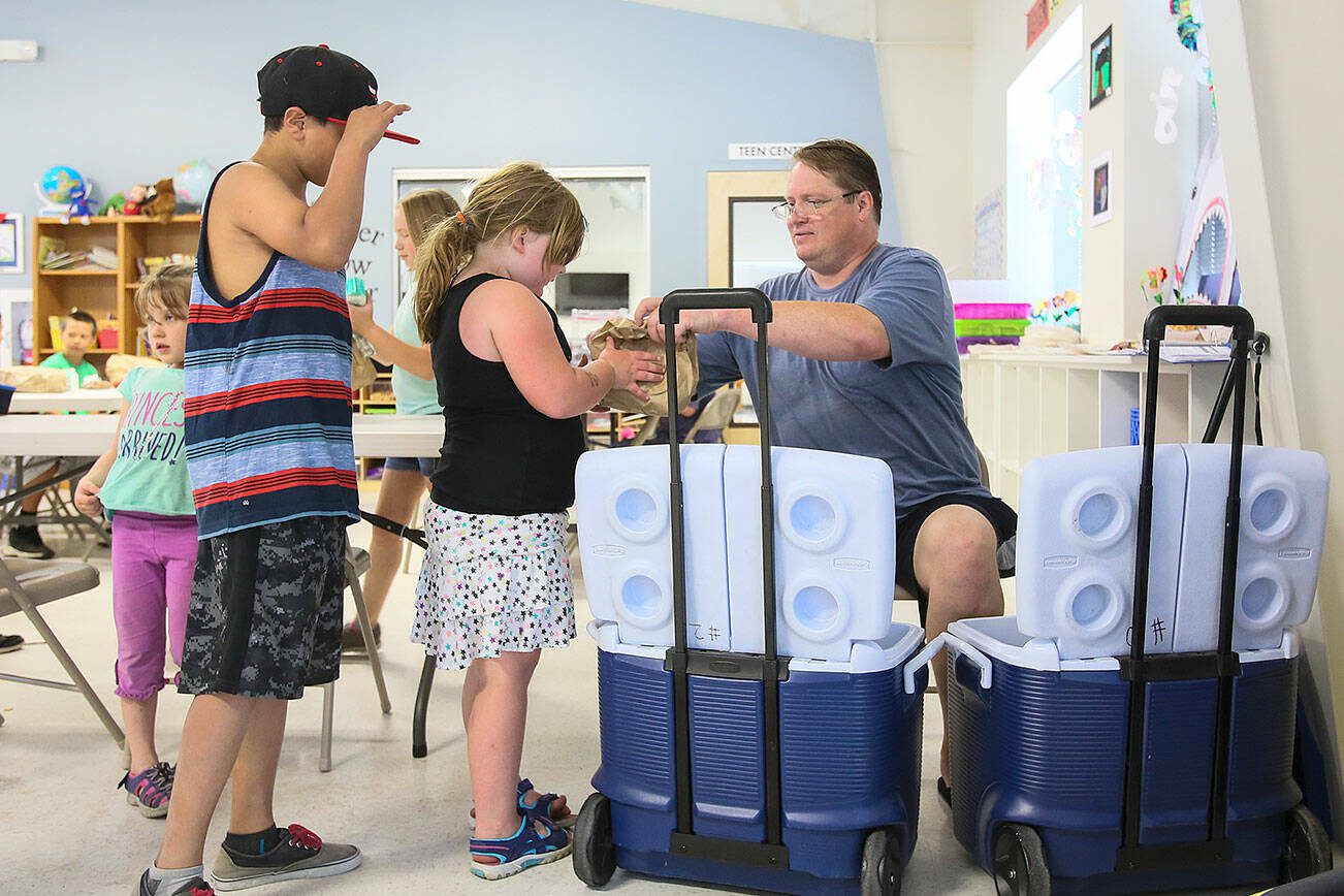 From one of two coolers, Mike Bradshaw-Heiberg hands out brown bag lunches and half pints of milk as part of the Kids Cafe summer meals program on July 1, 2015 in Sultan, Wa. (Kevin Clark / The Herald)