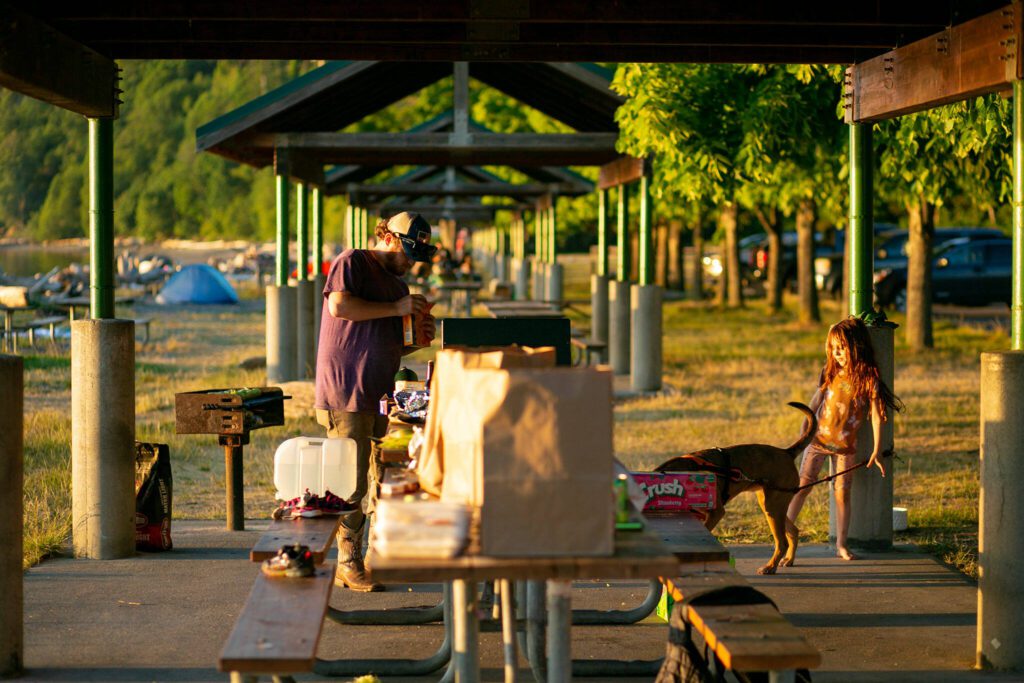 Charles Robbins pieces together a steak dinner for his family as young Athea Miller plays with the family dog, Lana, under one of the shelters at Kayak Point on Monday, June 12, 2023, in Stanwood, Washington. (Ryan Berry / The Herald)

