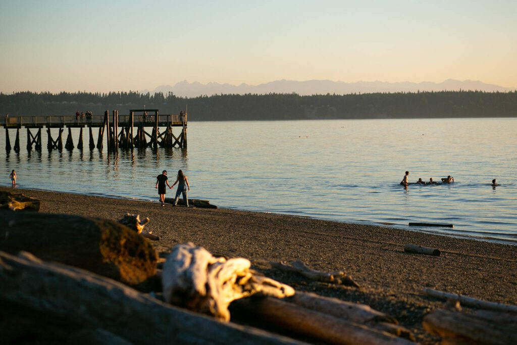 People fish from the pier, hold hands on the beach and steer a swamped canoe in the water as the sun sets on another day at Kayak Point on Monday, June 12, 2023, in Stanwood, Washington. (Ryan Berry / The Herald)
