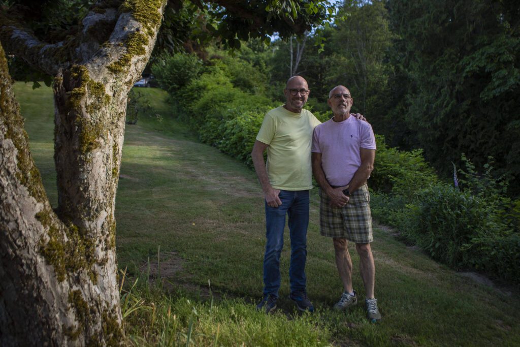 Doug Blay, left, and Tim Pfahl, right, pose for a photo at their home in Everett. They’ve had nine Pride flags stolen from their yard over two years. (Annie Barker / The Herald)
