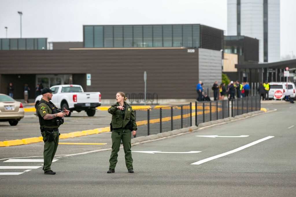 Two members of the Snohomish County Sheriff’s office direct traffic as TSA and other airport workers gather outside the terminal at Paine Field after the discovery of a suspicious package at the airport on Tuesday, June 13, 2023, in Everett, Washington. (Ryan Berry / The Herald)
