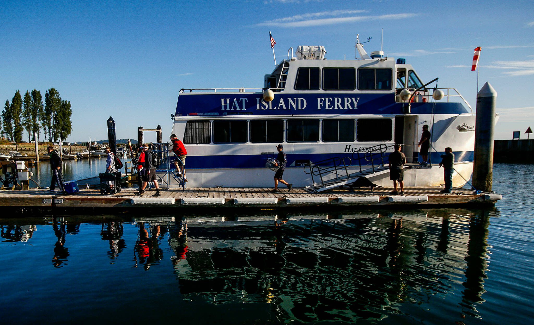 Islanders disembark the Hat Island Ferry, which is called the “Hat Express,” in 2018. At the top of the ramp stands Ray Brown, the captain. Below him on the dock are crew members Ryan Taisey, first mate (left) and Michael Jablinske. (Dan Bates / The Herald)