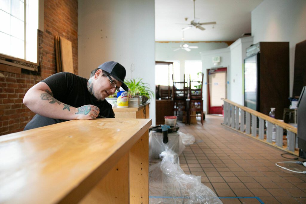 Adair Gearhart sands down a shelf while piecing together the future home of Catalyst Café on Tuesday, June 20, 2023, in downtown Everett, Washington. Gearhart has already moved out of Catalyst’s 23rd Street storefront and hopes the new location will evolve into a gathering place with more food and drink, longer hours, and even more resources and connections for the queer community. (Ryan Berry / The Herald)
