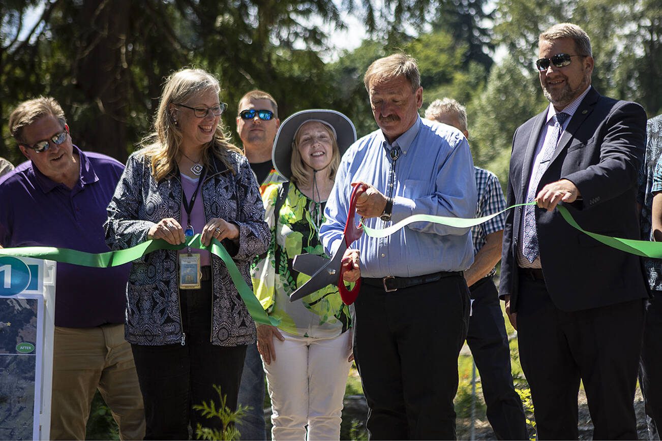 Snohomish County Executive Dave Somers, center, cuts a ribbon at a section of the Little Bear Creek Advance Mitigation Site near 58th Ave SE in Woodinville, Washington on Wednesday, July 12, 2023. (Annie Barker / The Herald)