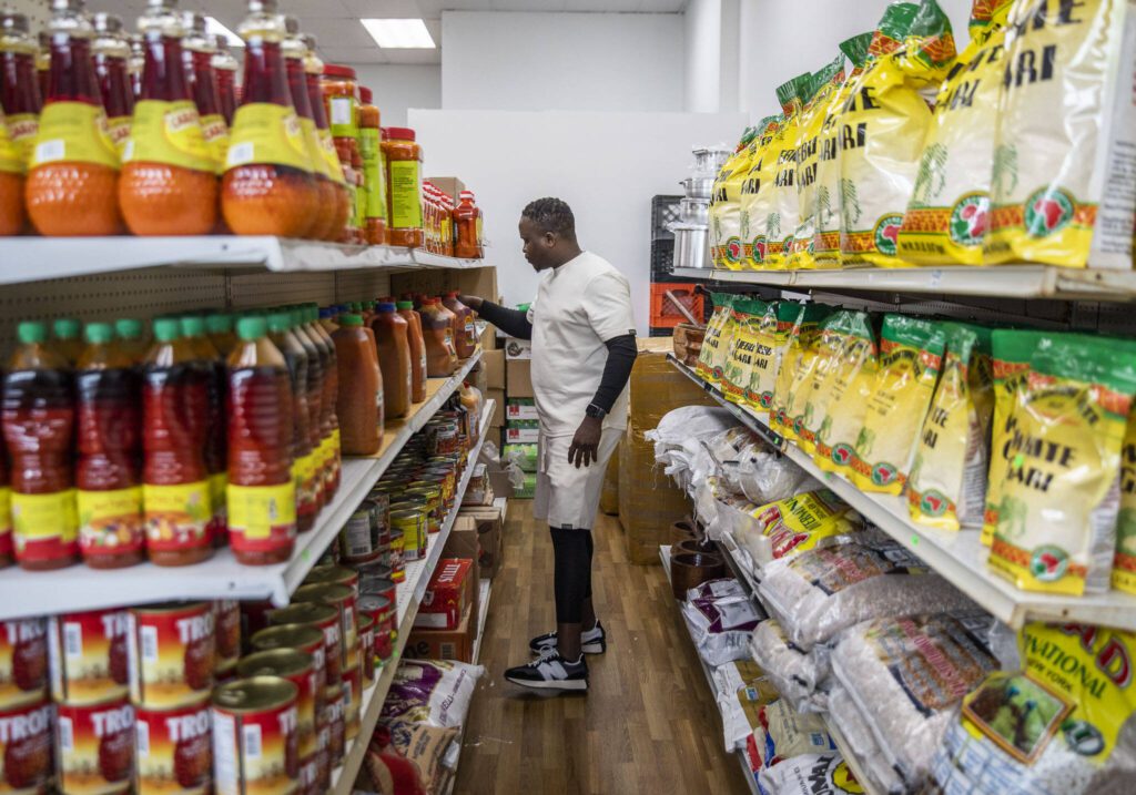 Yusupha Bojang grabs a jug of palm oil off of the shelf at his market on Wednesday, June 21, 2023 in Everett, Washington. (Olivia Vanni / The Herald)
