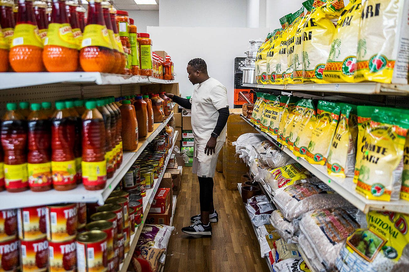 Yusupha Bojang grabs a jug of palm oil off of the shelf at his market on Wednesday, June 21, 2023 in Everett, Washington. (Olivia Vanni / The Herald)