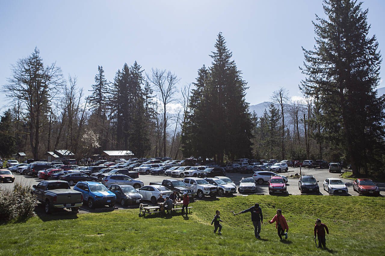 A family sits at a picnic table next to a full parking lot at the Wallace Falls State Park trailhead on a Saturday in March 2020, near Gold Bar. (Olivia Vanni / The Herald file photo)