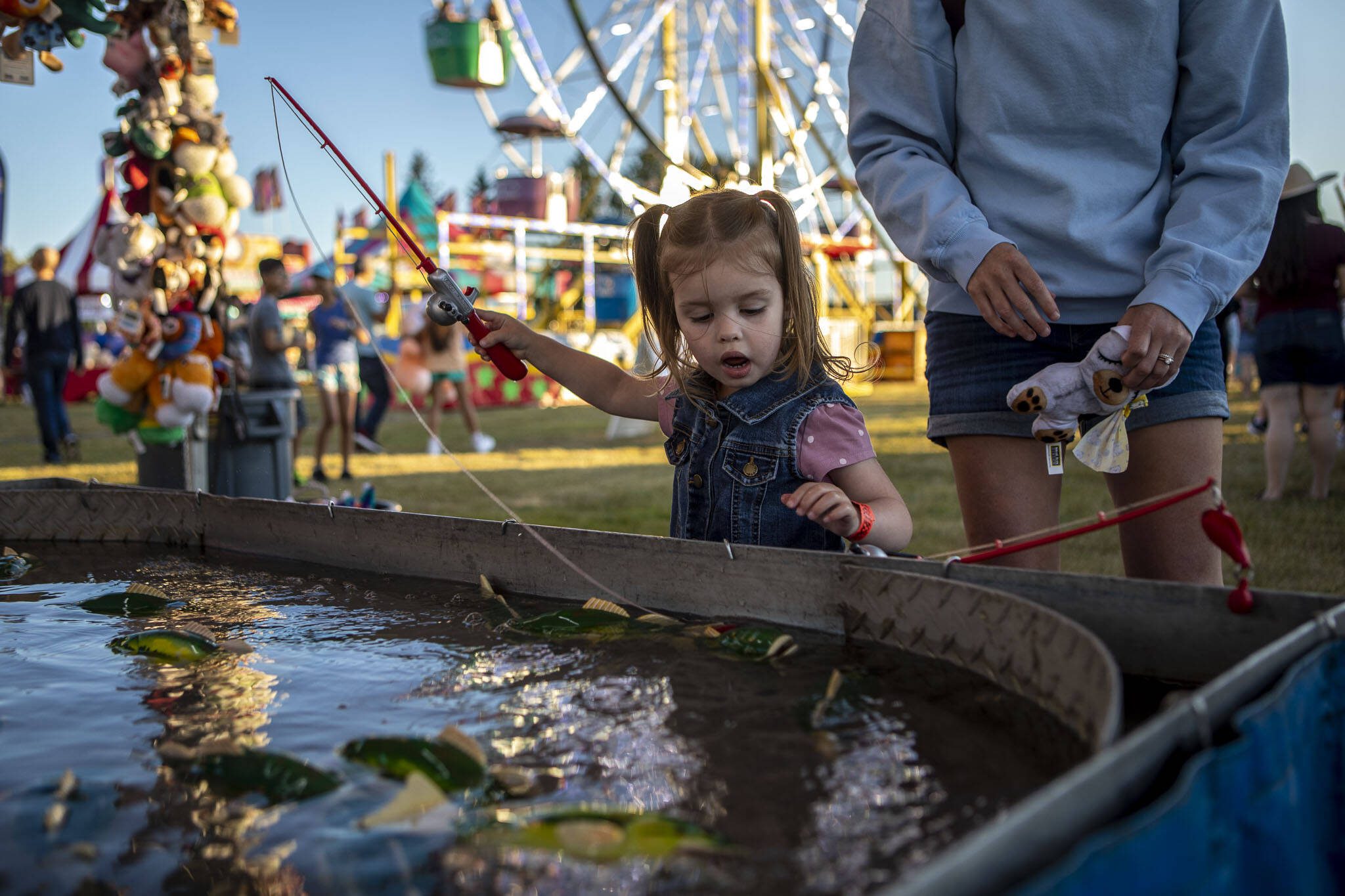 Emily Hillman, 2, left, secures a fish for a prize with their mom, Piper Hillman, 34, right, during the Kla Ha Ya Days carnival at Harvey Field in Snohomish, Washington on Thursday, July 13, 2023. (Annie Barker / The Herald)