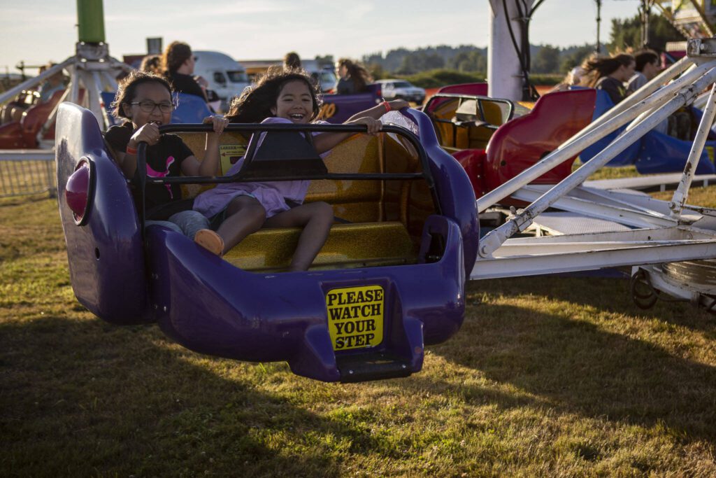 Keala Hew, 7, left, and Riley Alvarado, 7, right, smile on a ride during the Kla Ha Ya Days carnival at Harvey Field in Snohomish, Washington on Thursday, July 13, 2023. (Annie Barker / The Herald)
