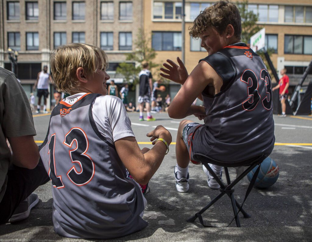 Ryder Hansen, 12, left, watches as Chase Lee, 12, right, jokingly flexes his muscles while waiting for their next game during the Everett 3on3 tournament Sunday in downtown Everett. (Annie Barker / The Herald)
