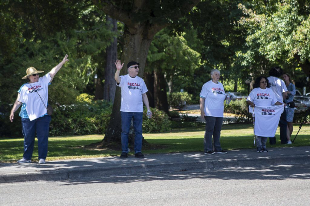 Individuals wear “Recall Binda” shirts and wave to cars passing by after a NAACP Snohomish County press conference at Lynnwood City Hall in Lynnwood, Washington on Thursday, July 20, 2023. (Annie Barker / The Herald)

