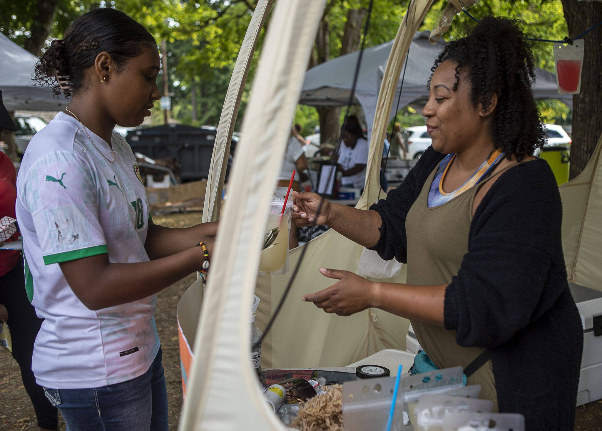 Tea Moss Shop Owner Takiyah Miller, right, serves a drink to a customer during the Nubian Jam at Forest Park in Everett, Washington on Saturday, July 29, 2023. (Annie Barker / The Herald)