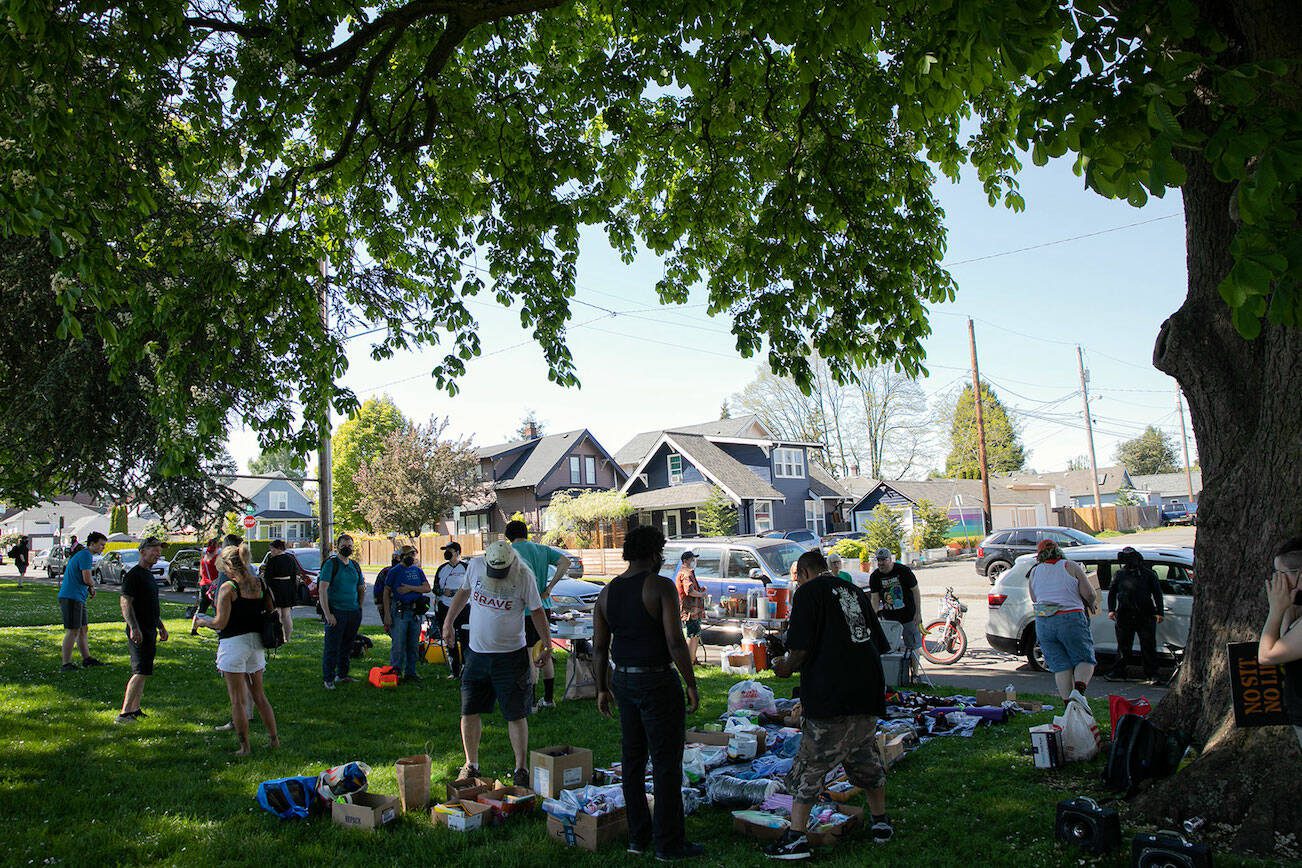 People gather in the shade during a community gathering to distribute food and resources in protest of Everett’s expanded “no sit, no lie” ordinance Sunday, May 14, 2023, at Clark Park in Everett, Washington. (Ryan Berry / The Herald)