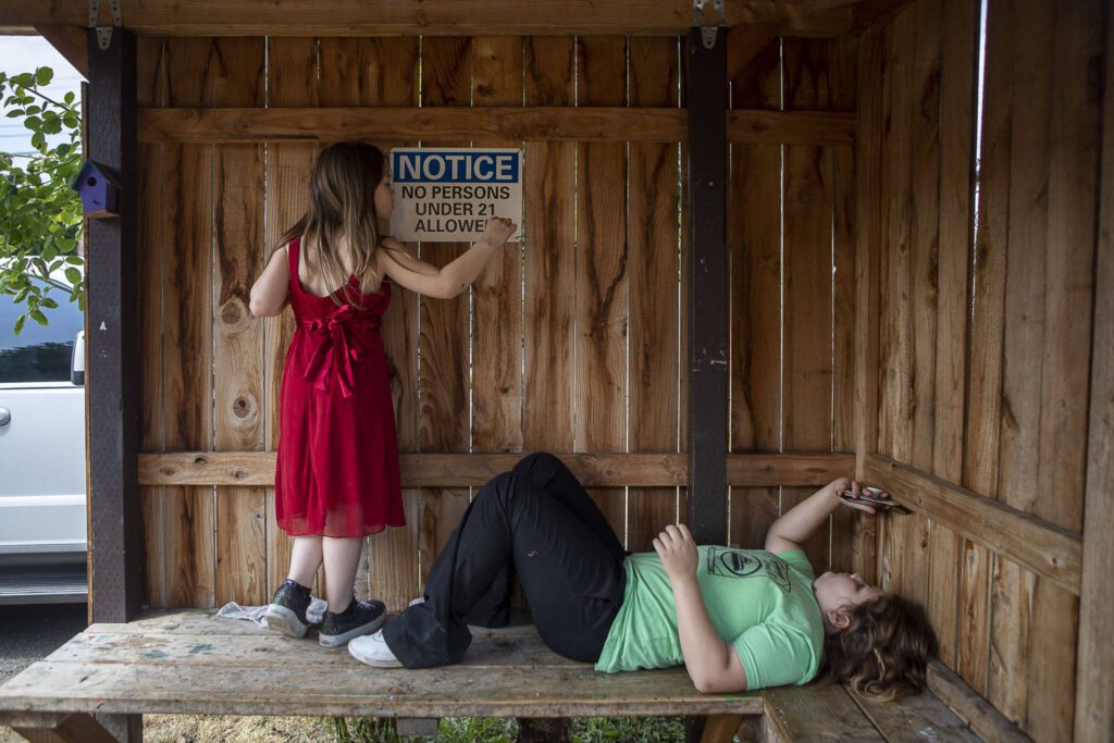 Mia Boucher, 9, playfully adds a sticker over the “2” in a notice that allows only 21-year-olds in the smoking area while her sister Makayla Boucher, 11, plays on a phone. (Annie Barker / The Herald)
