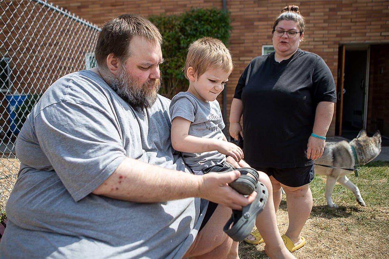 Marc Boucher, left, helps Maverick Boucher, 4, put on his shoes as Amanda Boucher, right, stands by to assist at the Interfaith Association of Northwest Washington located at 2520 Cedar Street in Everett, Washington on Sunday, July 30, 2023. (Annie Barker / The Herald)