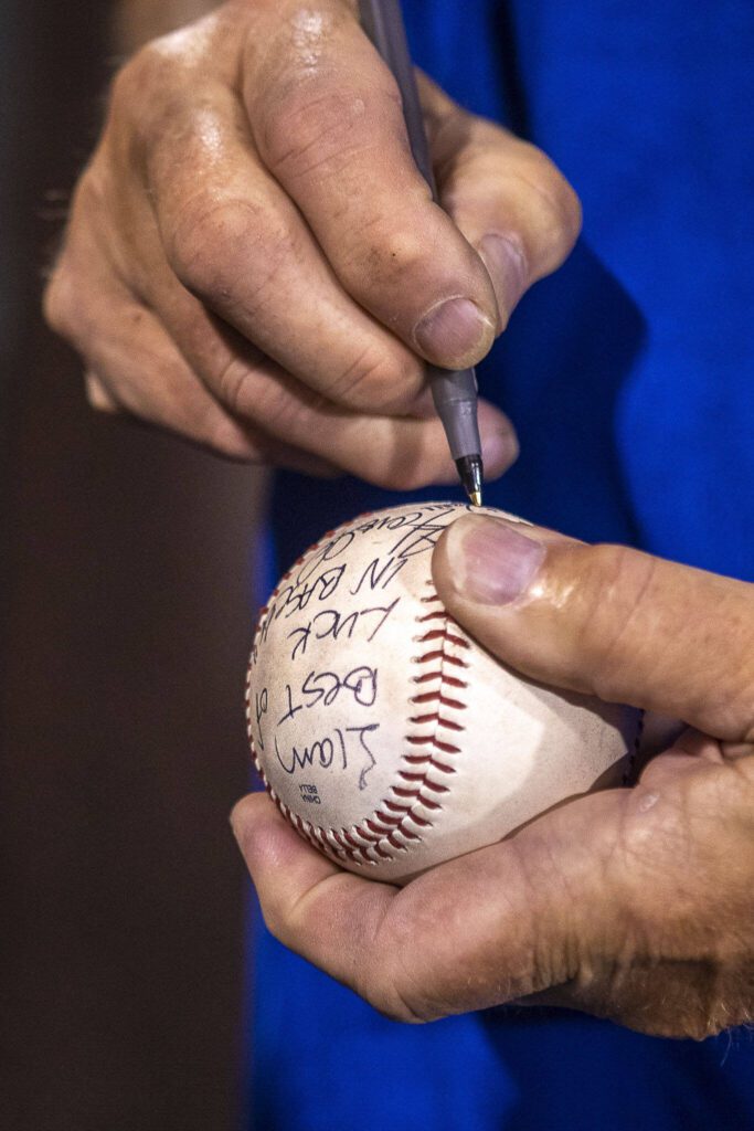 Everett Merchants manager Harold Pyatte signs a ball “Liam, best of luck in Baseball – Harold Pyatte” after his final game on Friday at Funko Field in Everett. (Annie Barker / The Herald)

