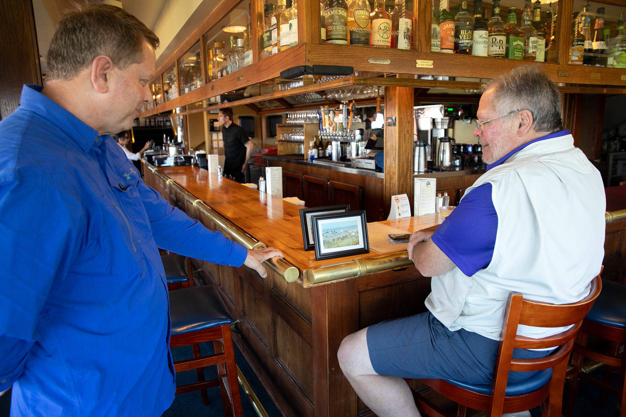 Arnies co-owner and longtime manager Rob Davis, left, chats with regular Kevin Armintrout at Arnies Pacific Northwest Favorites on Friday, August 11, 2023, in Mukilteo, Washington. Davis spoke fondly of countless regulars and staff who have built a community at the restaurant over the last 40 years including Armintrout, whose order is Tanqueray on the rocks with a lemon twist, and his late father, who preferred his gin neat with two olives. (Ryan Berry / The Herald)