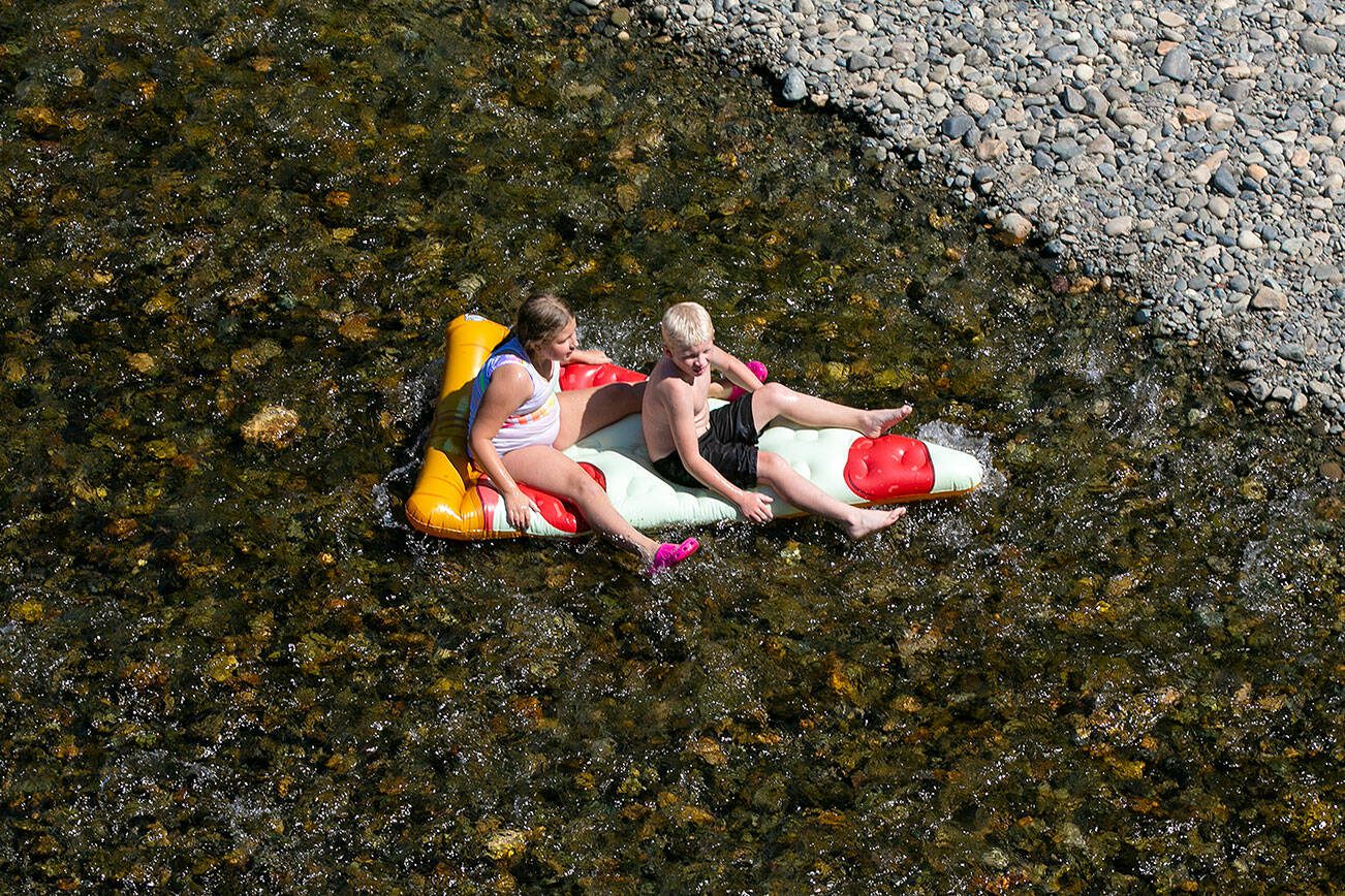 Two children float down the Pilchuck River on an inflatable slice of pizza on Sunday, August 13, 2023, in Snohomish, Washington. Inland temperatures look to creep into the 90s during the week. (Ryan Berry / The Herald)