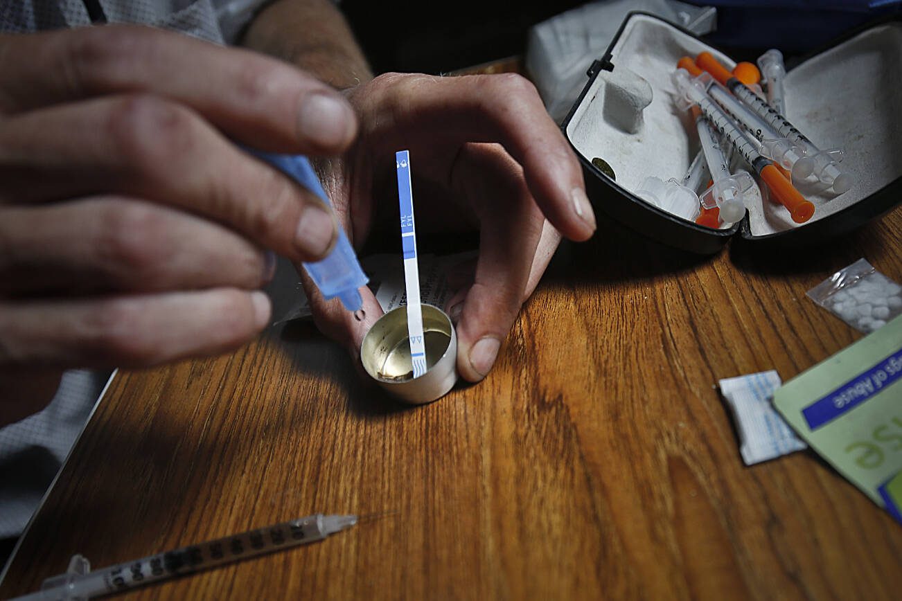An addict prepares heroin, placing a fentanyl test strip into the mixing container to check for contamination, Wednesday Aug. 22, 2018, in New York. If the strip registers a "pinkish" to red marker then the heroin is positive for contaminants. (AP Photo/Bebeto Matthews)