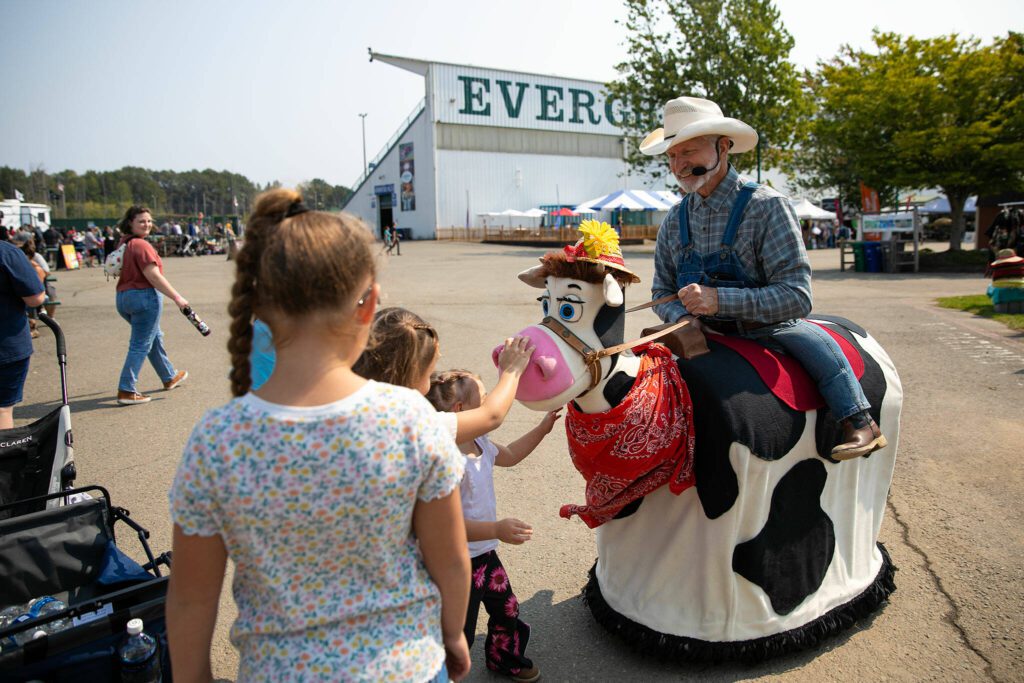 “Farmer Joe” Stoddard and Daisy the Talking Cow stop to chat with some kids during opening day of the Evergreen State Fair on Thursday, August 24, 2023, in Monroe, Washington. Stoddard puts on a one-man (and one-cow) comedy and music act and will be performing on stage during the fair. (Ryan Berry / The Herald)
