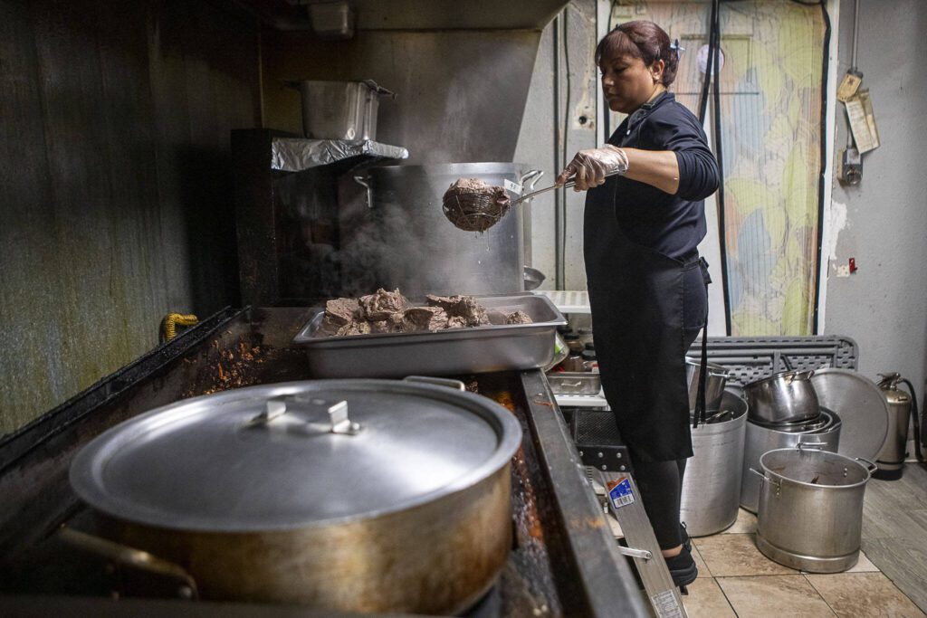 Prep team member Yolanda Jimenez removes beef used in the birria tacos from a large pot to cool down and be finely cut at El Mariachi in Everett, Washington on Wednesday, July 5, 2023. (Annie Barker / The Herald)
