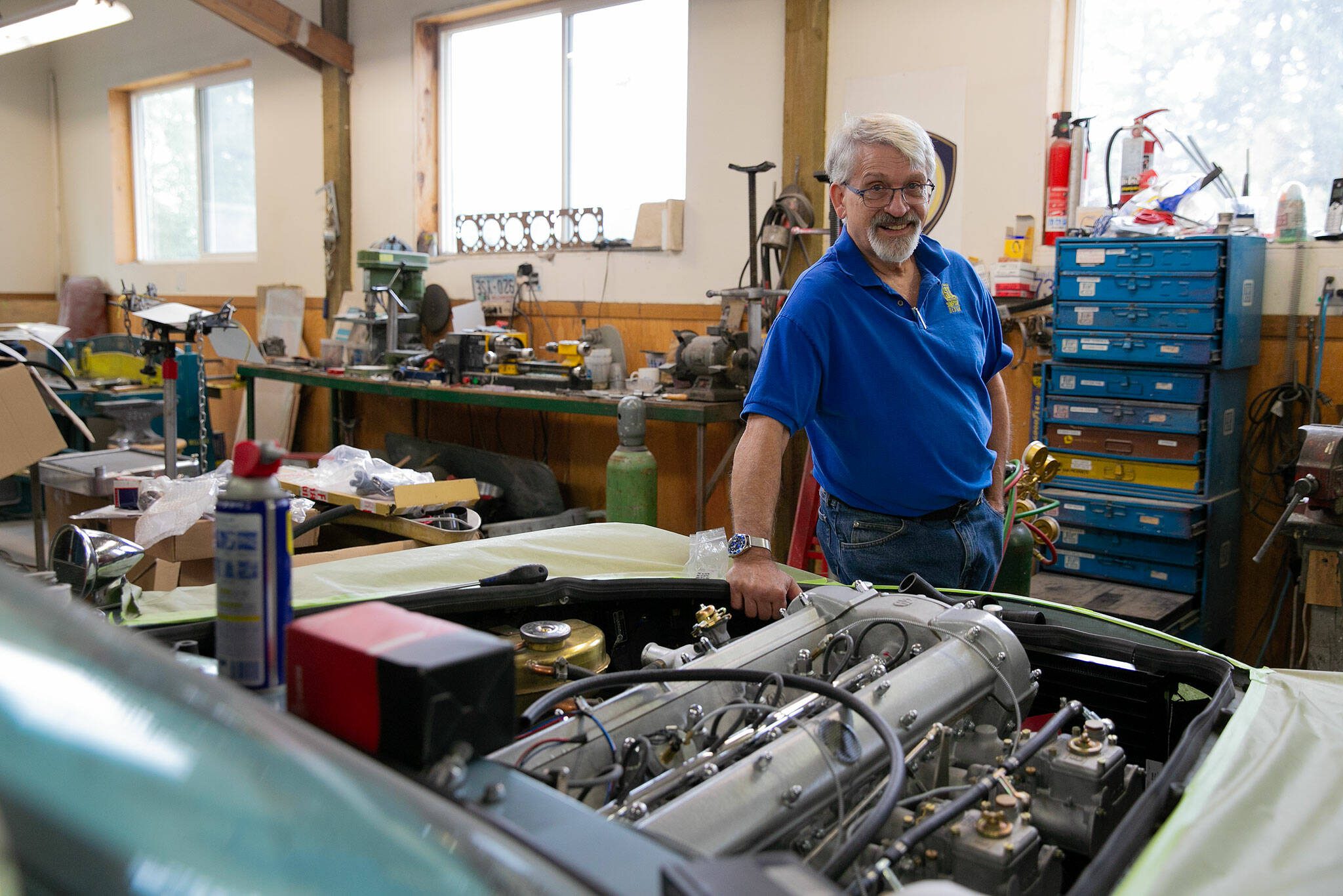 Jim Simpson, director of Simpson Design and Contemporary Classics of WA, stands over the hood of a 1966 Aston Martin DB6 that he has been restoring for a client over the last year on Friday, August 25, 2023, in Clinton, Washington. Simpson began his path into automotive work at the age of 13 when he was growing up in Texas. (Ryan Berry / The Herald)