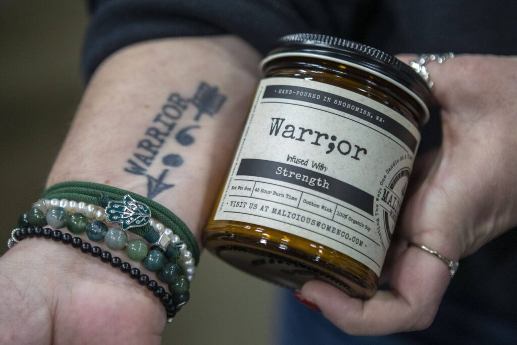 Owner and CEO Lacie Carroll holds a “Warr;or” candle at the Malicious Women Candle Co workspace in Snohomish, Washington on Wednesday, Feb. 15, 2023. The business is women run and owned. (Annie Barker / The Herald) 

