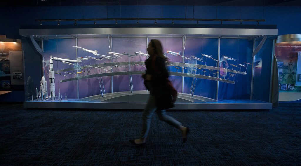 As a call to line up for the Boeing Assembly plant is called out, a tourist runs past a display of Boeing airplanes at the Future of Flight Museum in Everett, Washington. (Andy Bronson / The Herald)
