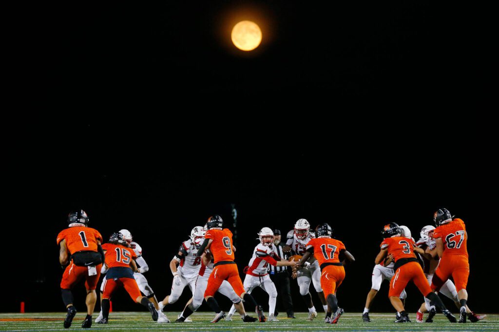 Mountlake Terrace’s Matthew Meadows hands the ball off to star running back Zaveon Jones as the Harvest Moon rises in the distance during a matchup against Monroe on Friday, Sept. 29, 2023, at Monroe High School in Monroe, Washington. (Ryan Berry / The Herald)
