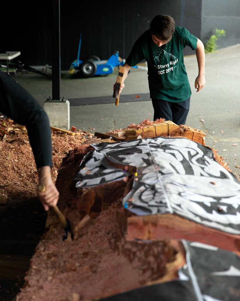 Junior Cory Maxwell takes a turn using an adze to chip away at a healing pol. (Ryan Berry / The Herald)
