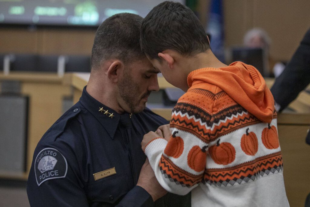 Andy Illyn, left, receives his badge from his son, Phoenix, right, as he is sworn in as the new Mukilteo Police Chief on Monday, Oct. 2, 2023. (Annie Barker / The Herald)
