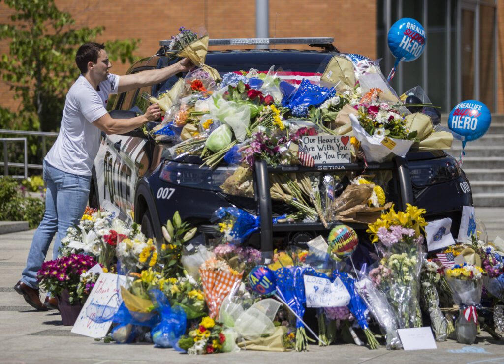 Tony Mandeville places a bouquet of flowers on the windshield of a Bothell Police Department vehicle that was turned into a memorial in front of Bothell City Hall on Tuesday, July 14, 2020 in Bothell, Wa. (Olivia Vanni / The Herald)
