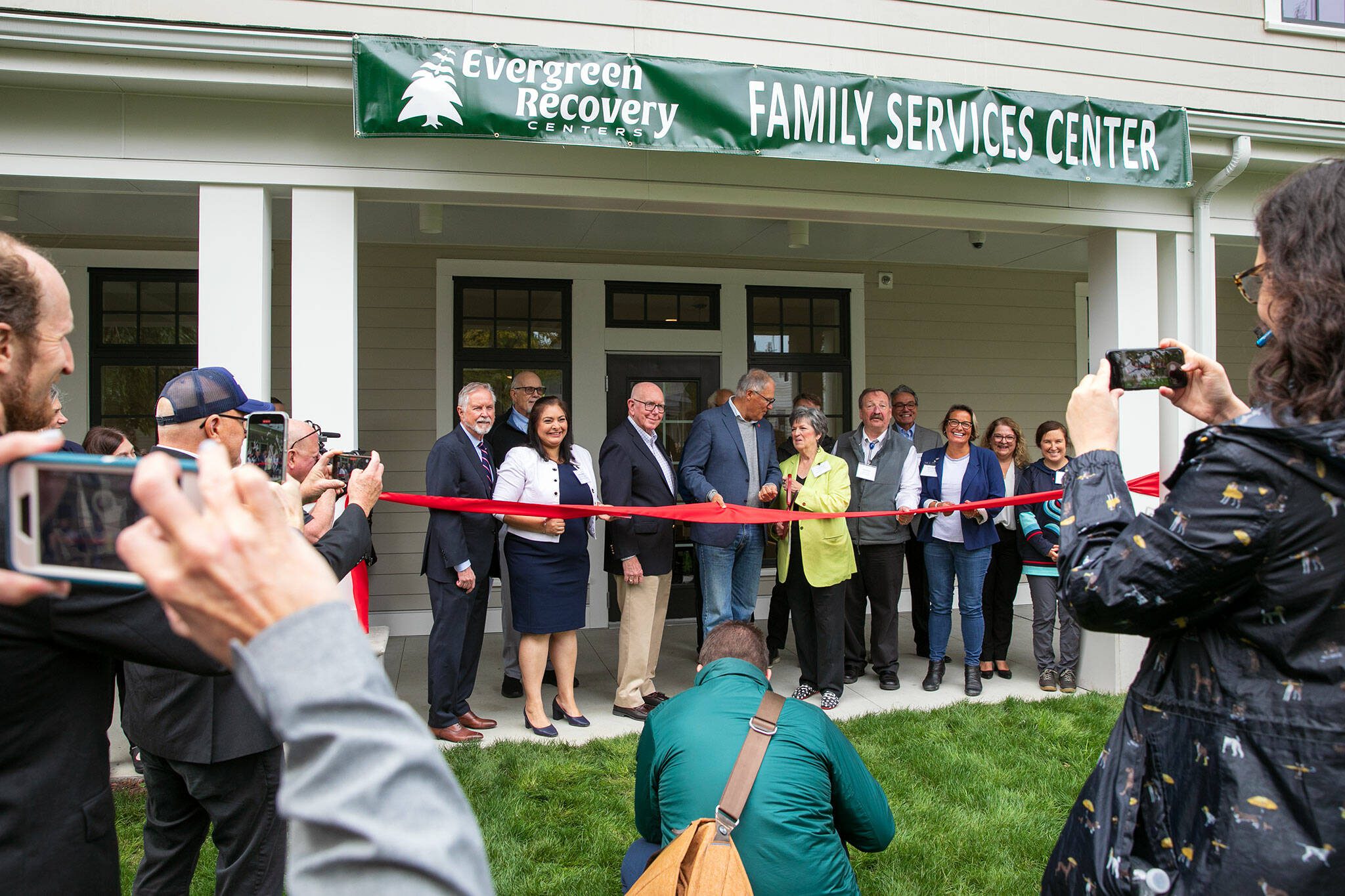 Gov. Jay Inslee and Evergreen Recovery Centers CEO Linda Grant, surrounded by others, cut the ceremonial ribbon during an event celebrating the Evergreen Manor Family Services Center on Tuesday, Oct. 10, 2023, in Everett, Washington. (Ryan Berry / The Herald)