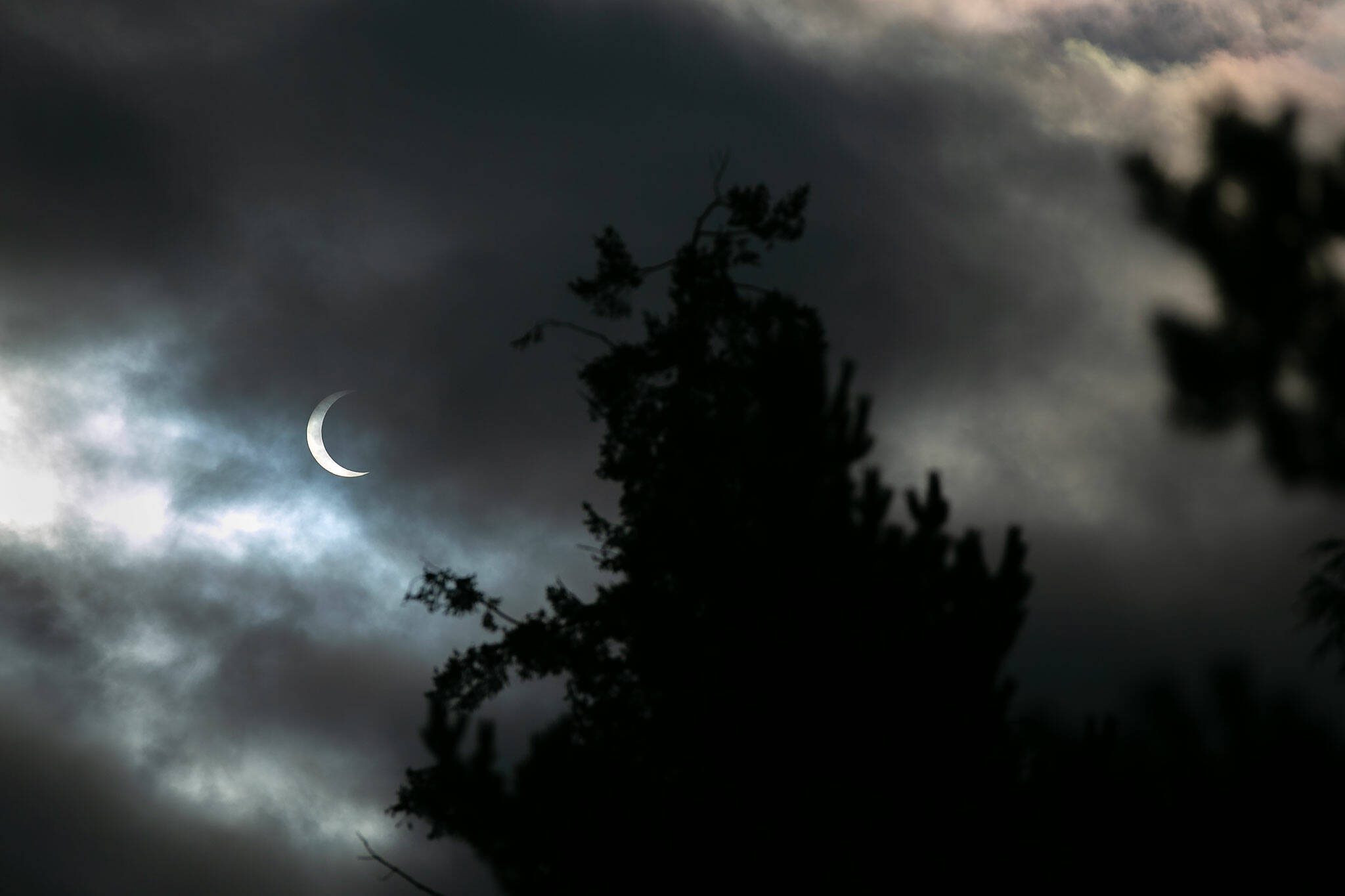 Clouds pass in front of the moon and sun as the two cross paths during an annular eclipse on Saturday, Oct. 14, 2023, seen from Everett, Washington. A total eclipse will be visible over parts of the United States in April 2024. (Ryan Berry / The Herald)