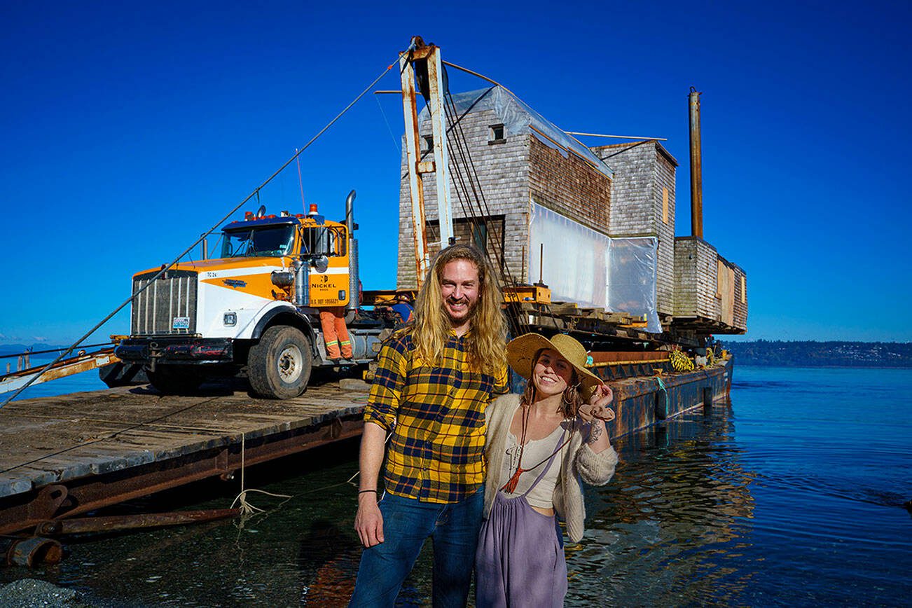 Tevon Dubois and Chanel Jost pose in front of their house as it is loaded onto a truck at a Possession Point dock on Oct. 13. (Photo by David Welton)