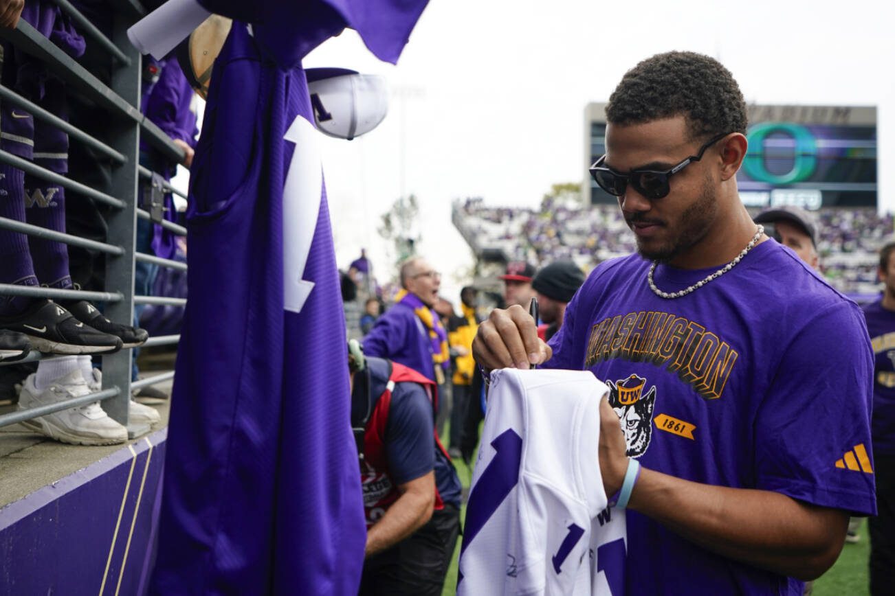 Seattle Mariners center fielder Julio Rodríguez signs autographs for fans on the sideline before an NCAA college football game between Washington and Oregon, Saturday, Oct. 14, 2023, in Seattle. (AP Photo/Lindsey Wasson)