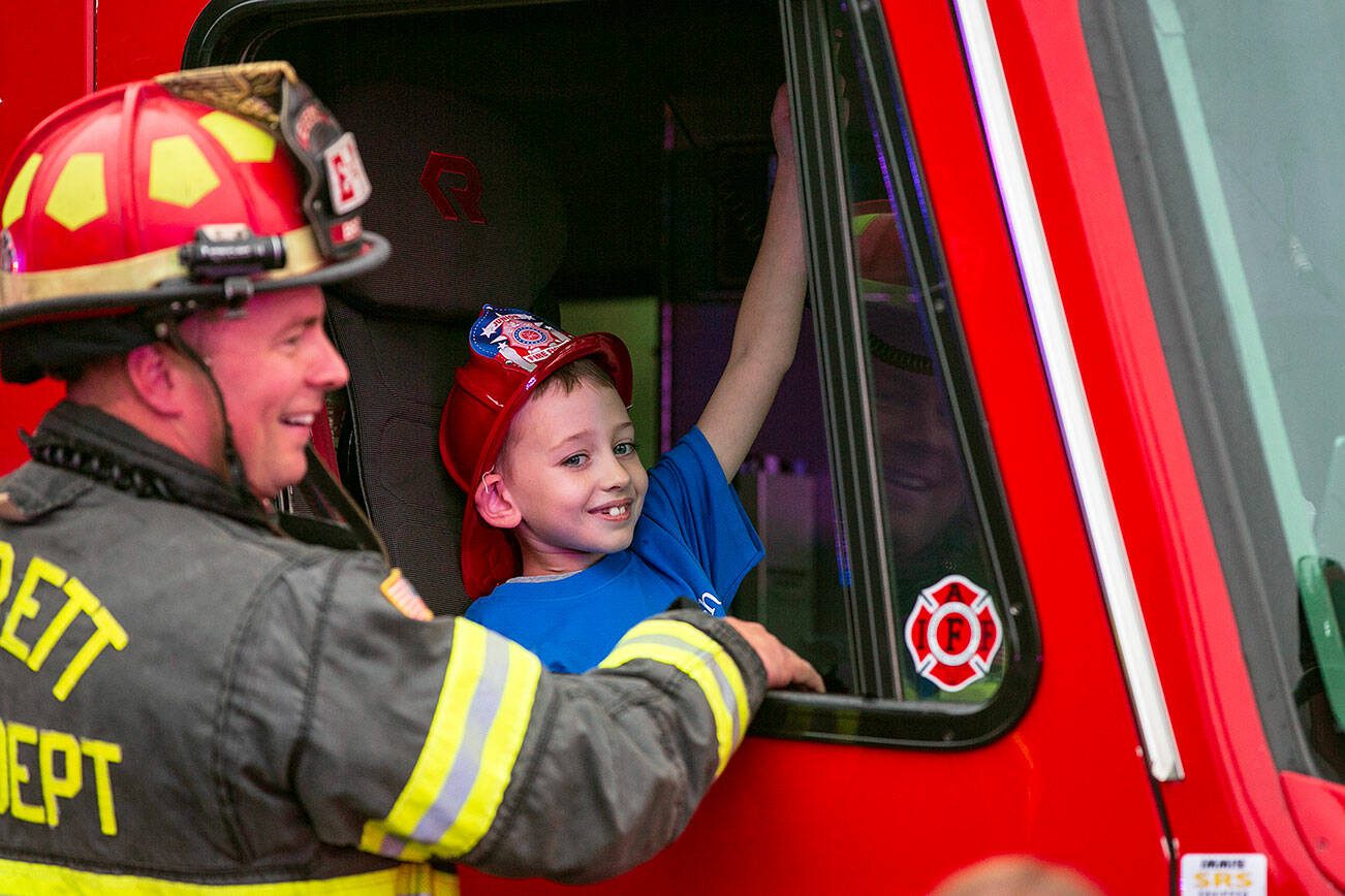 Carson gets a chance to sound the horn in an Everett Fire Department engine with the help of captain Jason Brock during a surprise Make-A-Wish sendoff Saturday, Oct. 21, 2023, at Thornton A. Sullivan Park in Everett, Washington. (Ryan Berry / The Herald)