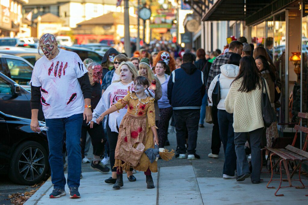 Pedestrians try to sneak by as a horde of zombies marches down First Street during the 10th annual Snohomish Zombie Walk on Saturday, Oct. 28, 2023, in downtown Snohomish, Washington. The yearly event acts a fundraiser for the Snohomish Community Food Bank. (Ryan Berry / The Herald)
