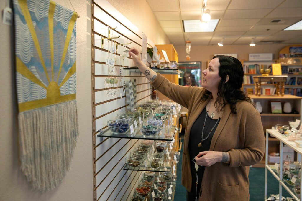 Visual merchandiser April Votolato hangs necklaces as workers at East West Books & Gifts stock shelves during the store’s third day in business Friday, Oct. 27, 2023, in Edmonds, Washington. (Ryan Berry / The Herald)
