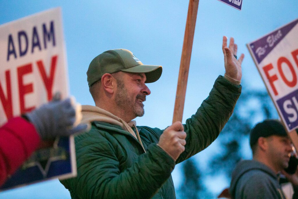 Snohomish County Sheriff Adam Fortney waves signs with supporters along Highway 9 on Monday, Nov. 6, 2023, in Arlington, Washington. (Ryan Berry / The Herald)
